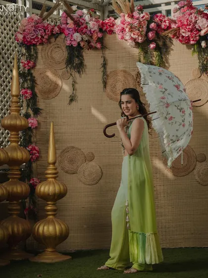 A bride in a lovely lime green outfit for her Mehendi ceremony, holding a parasol. This showcases our ability to capture beautiful portraits during daytime pre-wedding events.