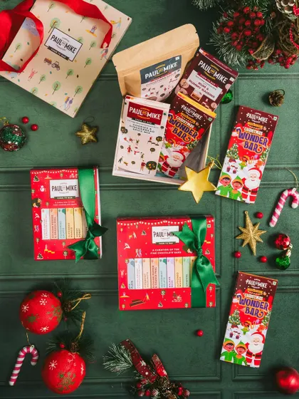 A dark and moody flatlay of Christmas-themed chocolate bars and gift boxes, using rich greens and reds to create a classic holiday feel.