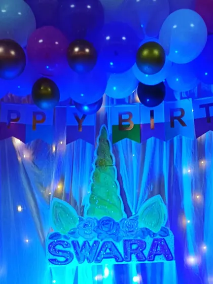 A magical unicorn theme for Swara's birthday. The centerpiece is a custom-made unicorn head with her name in glitter, set against a backdrop of blue balloons and twinkling fairy lights.