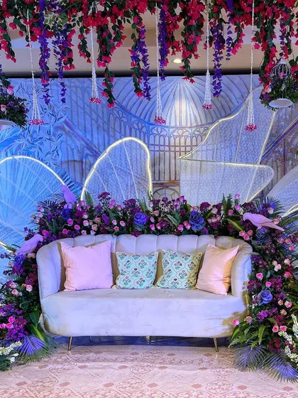 The seating backdrop in our 'Illuminated Garden' theme, featuring a custom-printed panel, neon-lit wings, and lush purple florals.