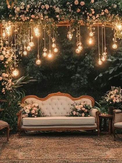 A cozy and rustic photo booth for a reception. The vintage sofa, floral arch, and hanging Edison bulbs create a warm and intimate spot for couple and guest photos.