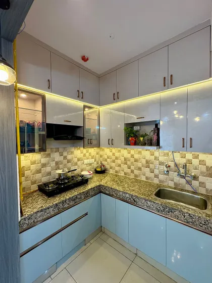 Another angle of the light blue modular kitchen, showing the placement of the sink and the overhead cabinets. The pendant light adds a decorative touch.