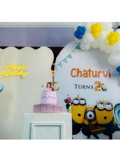 A fun and playful setup combining Dumbo and Minions for Chaturvi's second birthday. This decor features cute elephant cutouts, a Minions backdrop, and a simple white and yellow balloon arch.