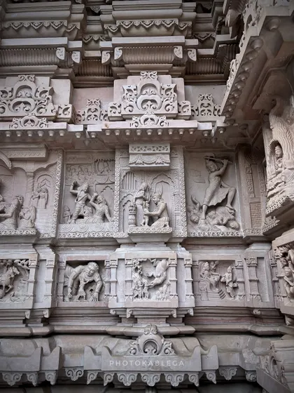 Detailed stone carvings on the wall of a temple at Govardhan Ecovillage, depicting scenes from Hindu mythology.