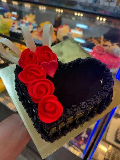 A dark chocolate heart-shaped cake with a basket-weave piping design. The red fondant roses and white chocolate ribbons add a touch of classic romance to this delicious cake.