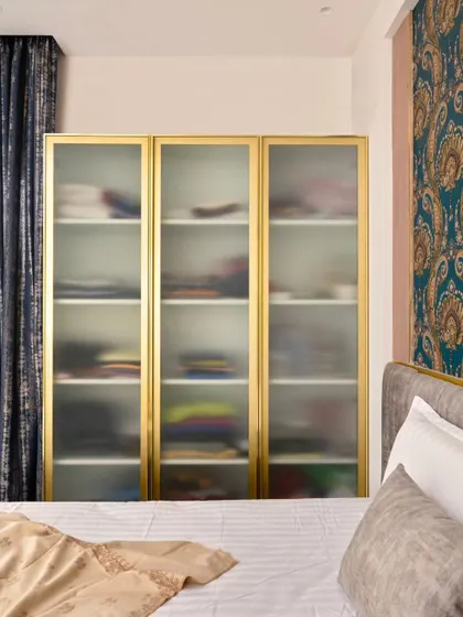 On the other side of the bed, a wardrobe with fluted glass and a gold aluminum frame provides semi-transparent storage, keeping the room from feeling too heavy.