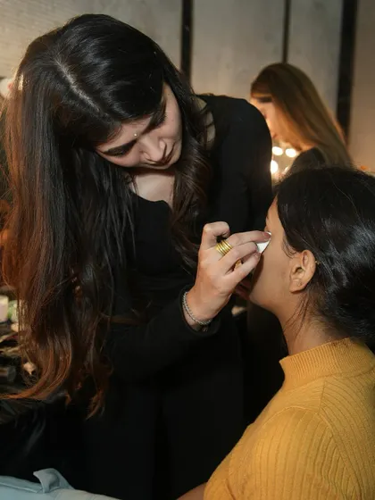 A student uses a cotton pad to perfect a model's eyeliner, demonstrating the attention to detail we instill in our artists.