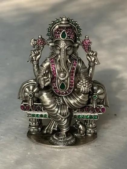 An antique-finish silver Ganesh murti, intricately detailed with pink and green stones. This piece combines traditional design with colourful accents, making it a unique addition to any collection.