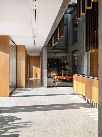 Sunlight casts dynamic shadows along the main corridor, where terrazzo floors meet exposed concrete and warm wood panels, creating a clean and bright circulation path.