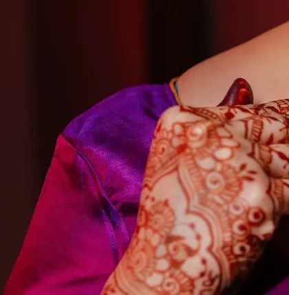 A close-up, artistic shot of a bride's hand, showing the intricate details of the henna stain against a vibrant purple saree.