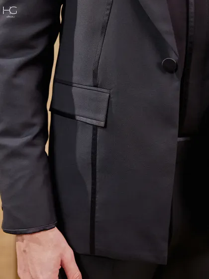A detail shot of the all-black suit, focusing on the piped pocket and the sleek, continuous lines that give the jacket its extraordinary character.