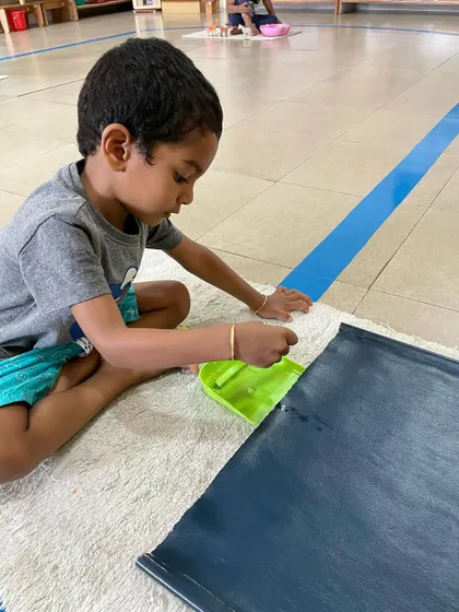 This child is engaged in a cleaning activity, using a small brush and pan. These tasks are not chores but are respected as important 'work' that builds skill and character.