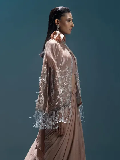 A side profile of a draped saree gown with a feathered jacket. This fusion look combines the elegance of a saree with the structure of a modern jacket.