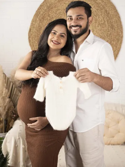 A sneak peek of what's to come. Holding up a tiny baby outfit is a classic and heartwarming way to celebrate the new life you are about to welcome.