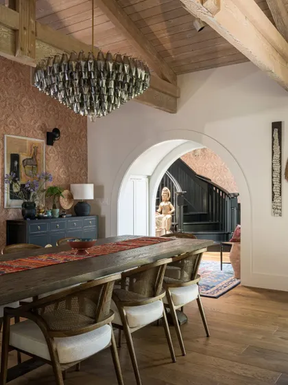 The dining area in the Saratoga home, featuring a stunning chandelier and wallpaper with a subtle, elegant pattern. The space blends rustic elements like the wooden table with more formal touches, creating a dining room that is both grand and welcoming.