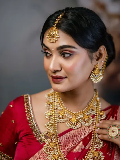 A model showcasing a layered antique gold necklace set with pearl details. This is a classic choice for a South Indian muhurtham ceremony.