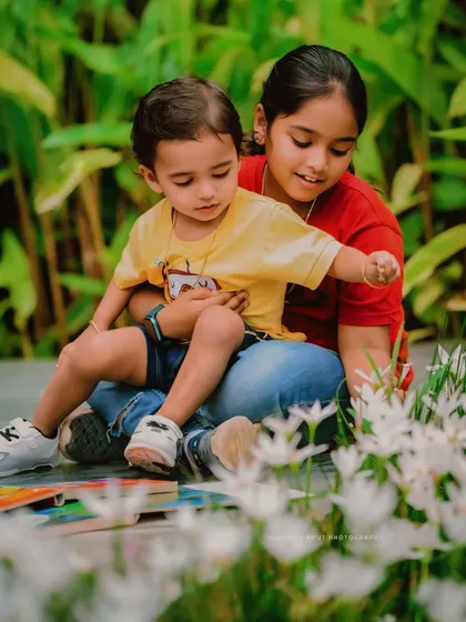 An older sister shows her younger brother something in the flowers. This is a beautiful, candid moment of sibling curiosity and connection during an outdoor shoot.