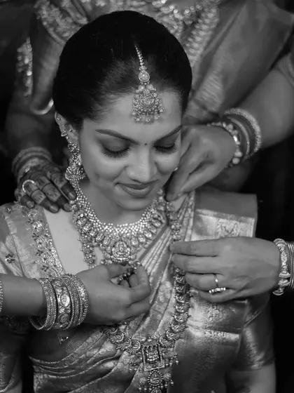 A beautiful black and white shot showing the hands of family members helping the bride with her necklace, symbolizing love and support.