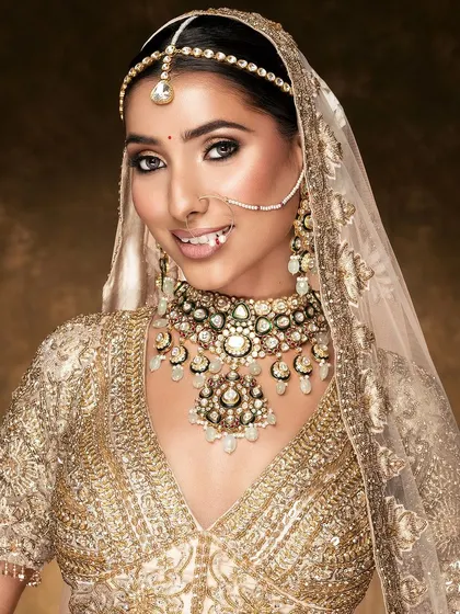 A joyful and radiant bridal portrait. The model's bright smile brings a wonderful energy to the image, complementing the magnificent gold and mint green jewelry and the heavily embroidered outfit.