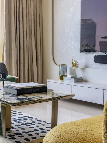 This shot highlights the details of the living room, including the marble coffee table, textured TV wall, and plush yellow armchair, creating a versatile and adaptable interior.