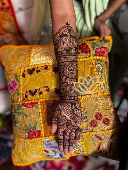 A single arm shot of a detailed bridal mehendi, featuring an Ambari elephant and other traditional motifs, resting on a colorful pillow.