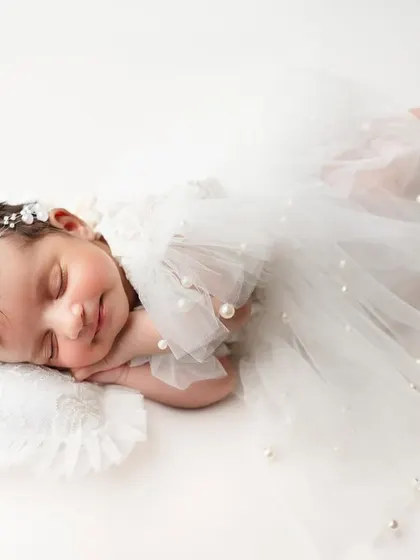 The most gorgeous sleeping beauty. Dressed in a delicate white tulle outfit, this baby looks like a tiny angel, captured against a clean, simple background.