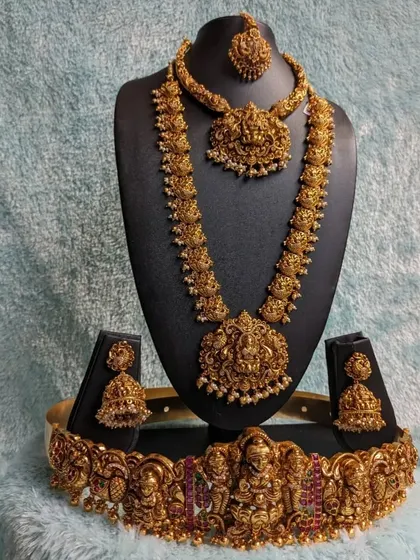 This is a full bridal set for the bride who wants it all. It includes an antique temple jewellery choker, a long haara, a maang tikka, jhumkas, and a matching hip belt, ensuring a grand and cohesive look.