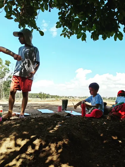 After the hard work of harvesting clay, some children take time to paint and draw in the shade, inspired by the natural surroundings.