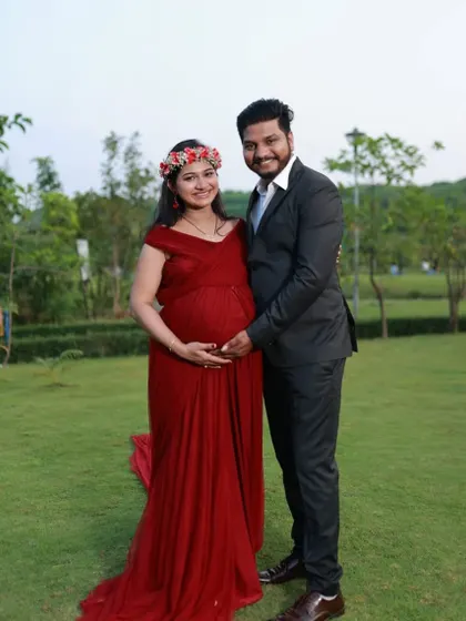 A happy couple posing in a park. The mom-to-be is wearing a wine-colored A-line gown with a small train, a comfortable and classic choice for an outdoor shoot.
