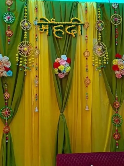 A beautifully draped Mehendi backdrop using yellow and green fabric, accented with small floral bouquets and wheel-shaped hangings.