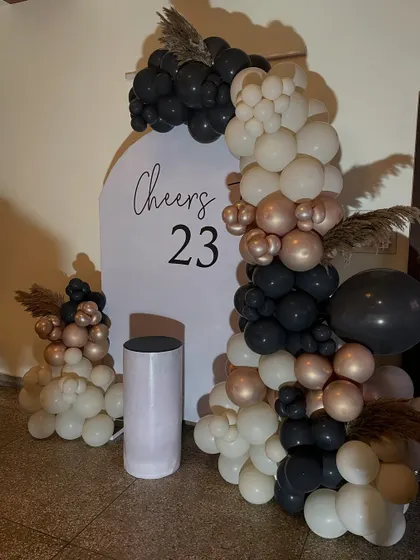 An elegant "Cheers to 23" birthday setup, featuring a modern balloon arch in black, white, and rose gold.