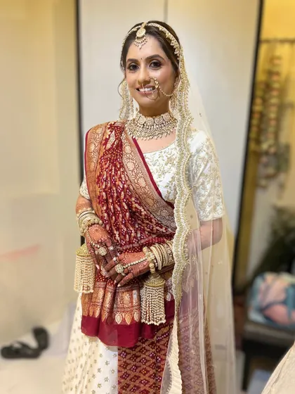 A full shot of the bride in her white and red Gujarati panetar. The makeup is classic and elegant, with a focus on defining her features.