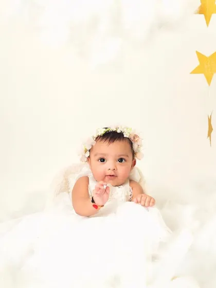 A little angel among the clouds and stars. The simple white dress and floral headband create a pure and innocent look.