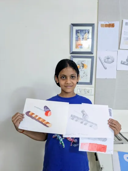 This student is holding her completed object studies, one in watercolor and the other in pencil. We encourage exploring the same subject in different mediums to understand how each can be used to show form and texture.