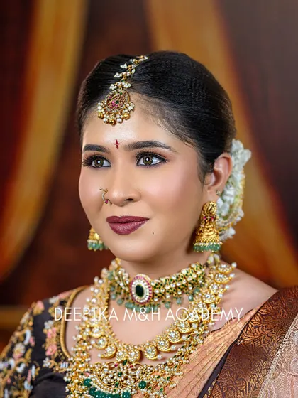 A close-up portrait focusing on the bride's face. The details of the maang tikka, nose ring, and layered necklaces are clearly visible, showcasing perfect accessorizing.