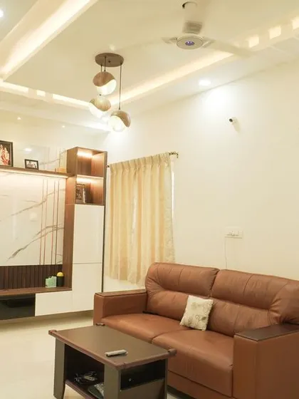 A spacious living room with a brown leather sofa and a modern TV unit. The unit features a marble back panel and a combination of open and closed storage.