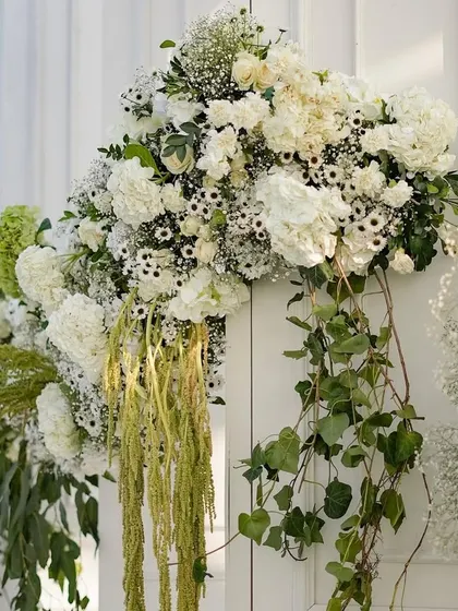 A close-up of the entrance florals, showing the mix of white hydrangeas, roses, and trailing greenery. The arrangement feels both luxurious and naturally beautiful.