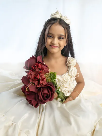 A beautiful portrait of a seven-year-old girl for her pre-birthday shoot. She looks like a princess in her elegant white gown, holding a bouquet of flowers.