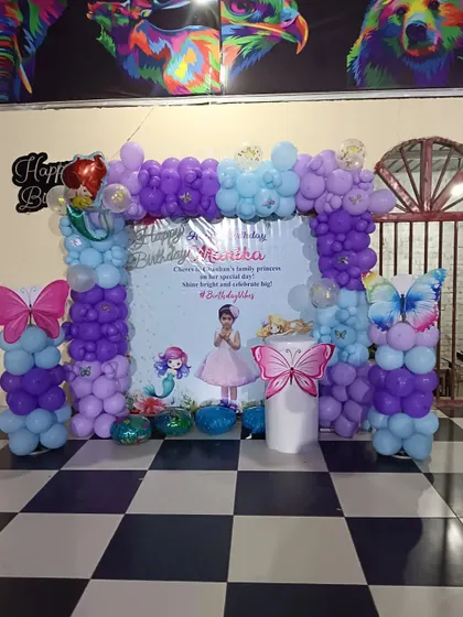 A butterfly and mermaid theme for a 6th birthday. This setup includes a custom backdrop with the birthday girl's photo, a purple and blue balloon frame, and large butterfly cutouts.
