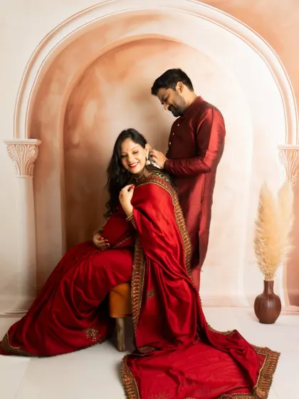 A classic seated portrait of a couple in matching traditional red outfits, creating a regal and coordinated look.