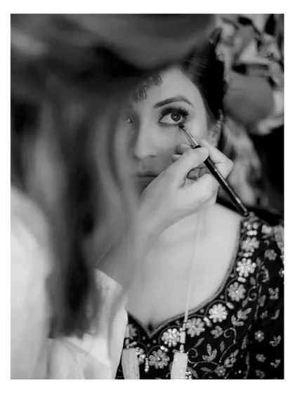 A behind-the-scenes, black and white shot of the bride's makeup being applied, capturing the quiet anticipation.