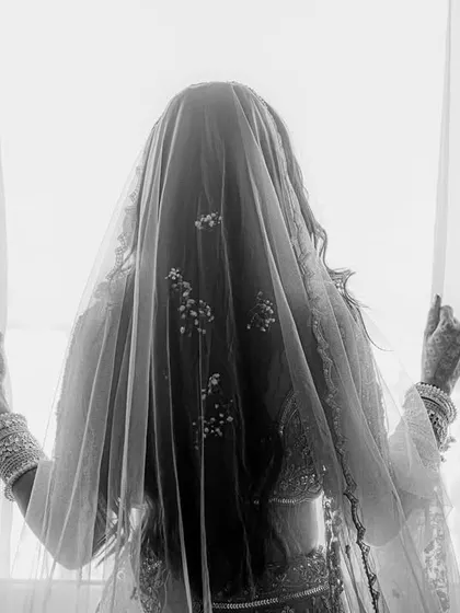 A serene black and white portrait of the bride looking out a window. Her back is to the camera, her form veiled, creating a moment of quiet contemplation.