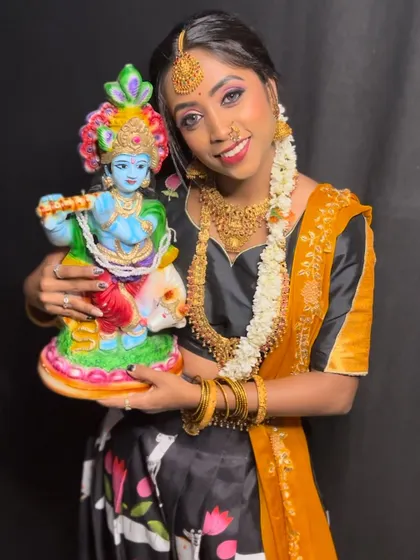 A smiling client holding a Krishna idol, dressed in a beautiful black, yellow, and orange Langa Davani.