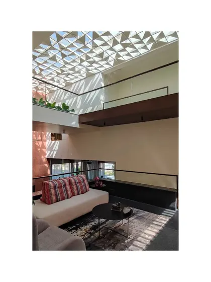 The living area of the Notan Home, seen from an upper level, showcases a dramatic geometric skylight that casts intricate patterns of light and shadow. This feature serves as a focal point, transforming the ceiling into a work of art.
