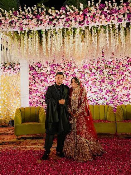 Another stunning shot of the couple on their floral stage. The rich red of the bride's lehenga contrasts beautifully with the pink and purple flowers, making for a vibrant and memorable photo.