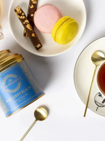 This top-down flat lay of Earl Grey tea is styled for a modern, elegant brand. The clean white space, paired with colourful macarons and gold spoons, creates a sophisticated image ideal for social media or a brand lookbook.