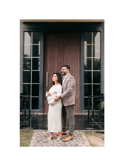 An expecting couple posing outdoors in front of a modern building with large glass-paned doors. This shot blends natural light with contemporary architecture for a stylish maternity portrait.
