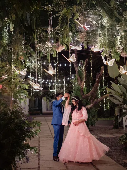 A fairytale-like engagement shoot at night. The couple dances under trees adorned with fairy lights and butterfly decorations, creating a truly magical and romantic scene.