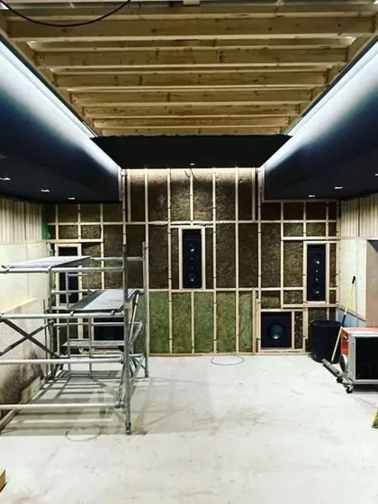 The front wall during construction, showing the in-wall speakers and subwoofers being installed into the wooden frame before being covered.