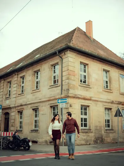 A full-shot of the couple walking across the street, capturing the beautiful European architecture and the feeling of being in a different world.
